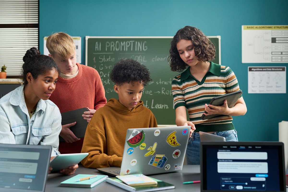 Teens collaborating on a laptop in a classroom while one explains a concept to classmates